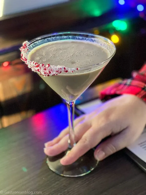 hand holding chocolate cocktail in martini glass with peppermint candy on rim