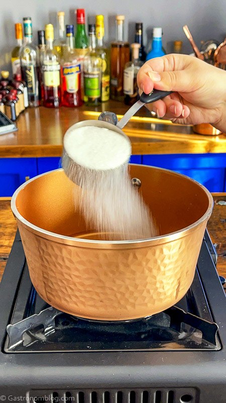 sugar being poured from measuring cup into copper saucepan