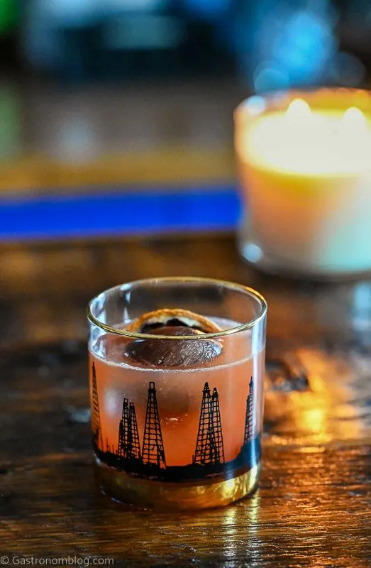 Pink Blood Orange Whiskey Sour cocktail in black oil rig printed rocks glass, candle in background