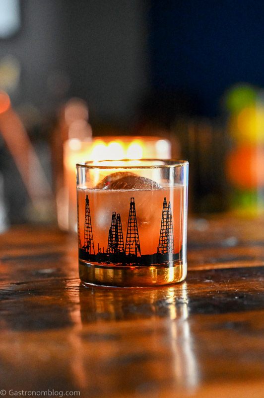 Pink Blood Orange Whiskey Sour cocktail in black oil rig printed rocks glass, candle in background