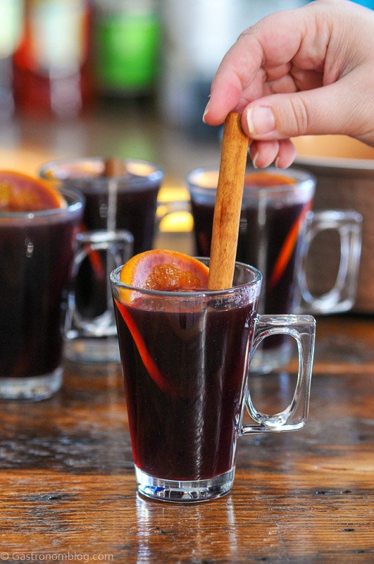 Red juice non alcoholic mulled wine in glass mugs with orange slices, hand placing a cinnamon stick