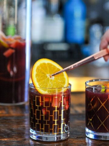 Tongs placing an orange into a gold glass with purple non alcoholic sangria