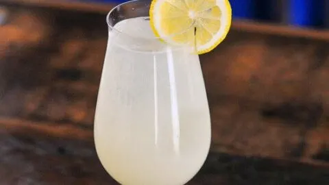 Yellow lemon non alcoholic spritzer ocktail in wine glass with straw and lemon wheel