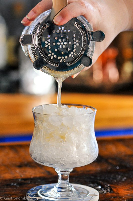 Gold liquid being poured into glass with crushed ice, a Winter Mai Tai cocktail