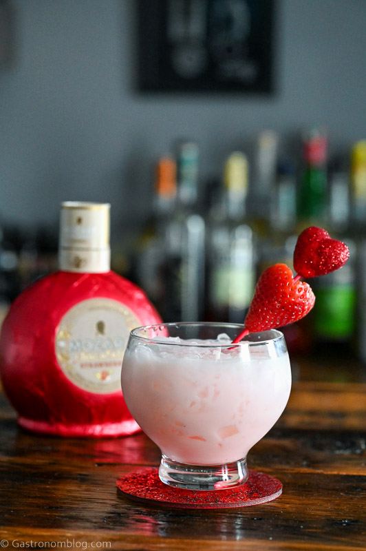Pink cocktail with strawberry on heart pick, this Strawberry Vodka Cocktail has Strawberry Liqueur bottle behind
