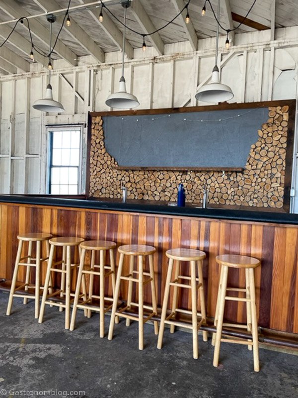 Bar inside hangar at Humboldt Bay Social Club, bar stools and wooden bar, with a wood backbar