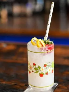 Vodka Spritzer cocktail in strawberry print glass with strawberry, lemon peel and straw