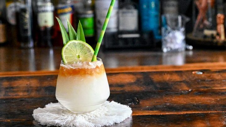 Mai Tai cocktail with dark rum layer on top with lime and pineapple fronds. On white coaster.