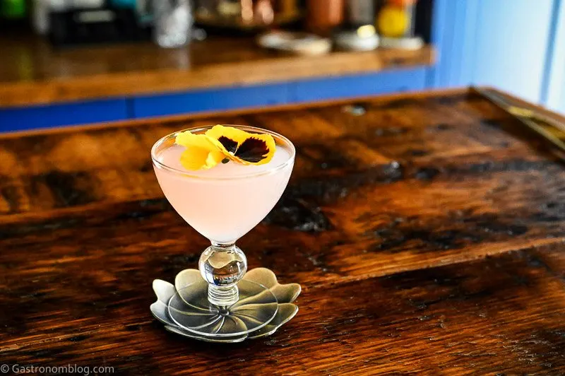 Pink Lilac Gimlet cocktail in coupe with yellow flower on silver coaster