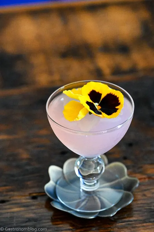 Pink Lilac Gimlet cocktail in coupe with yellow flower on silver coaster