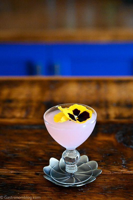 Pink Lilac Gimlet cocktail in coupe with yellow flower on silver coaster