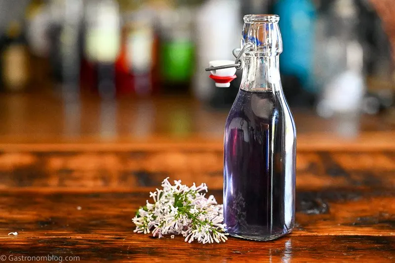 purple lilac simple syrup in a bottle, lilacs next to bottle on wood table