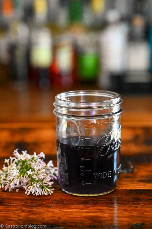 purple lilac simple syrup in a bottle, lilacs next to jar on wood table