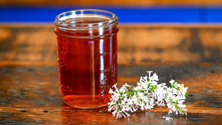 Pink lilac liqueur in jar with lilac flowers, on wood table