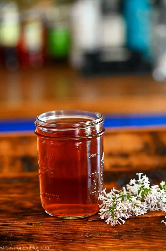 Pink lilac liqueur in jar with lilac flowers, on wood table