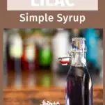 purple lilac simple syrup in a bottle, lilacs next to bottle on wood table