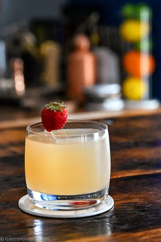 Light Pink strawberry syrup cocktail with whiskey and mezcal with a strawberry garnish