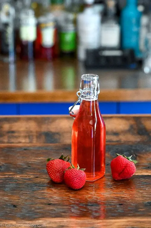 Red Strawberry Simple Syrup in a jar with strawberries around on a wooden table