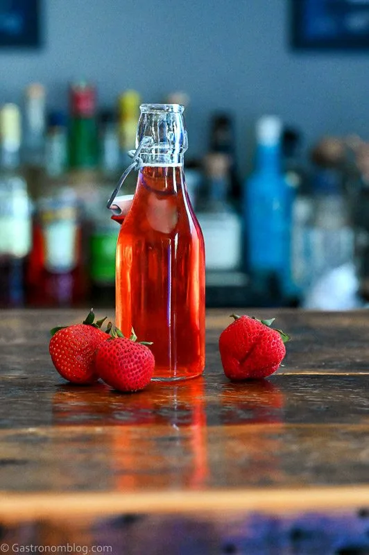 Red Strawberry Simple Syrup in a jar with strawberries around on a wooden table