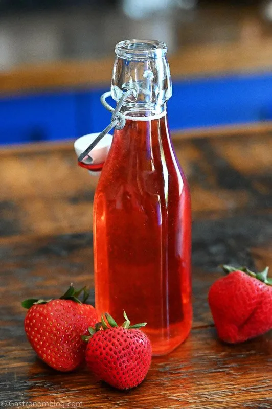 Red Strawberry Simple Syrup in a jar with strawberries around on a wooden table