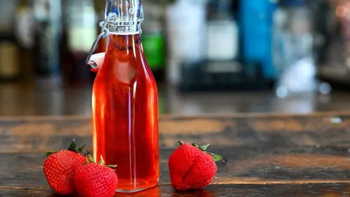 Red Strawberry Simple Syrup in a jar with strawberries around on a wooden table