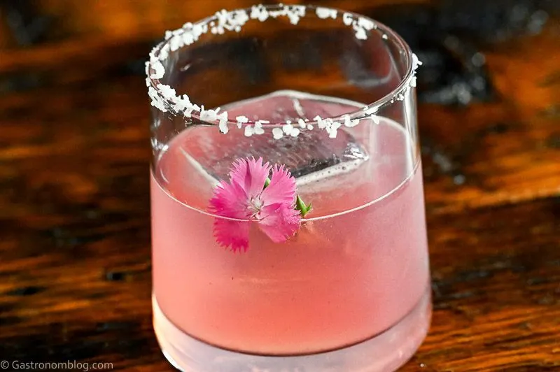 pink blackberry margarita cocktail in rocks glass with salt rim and pink flower garnish