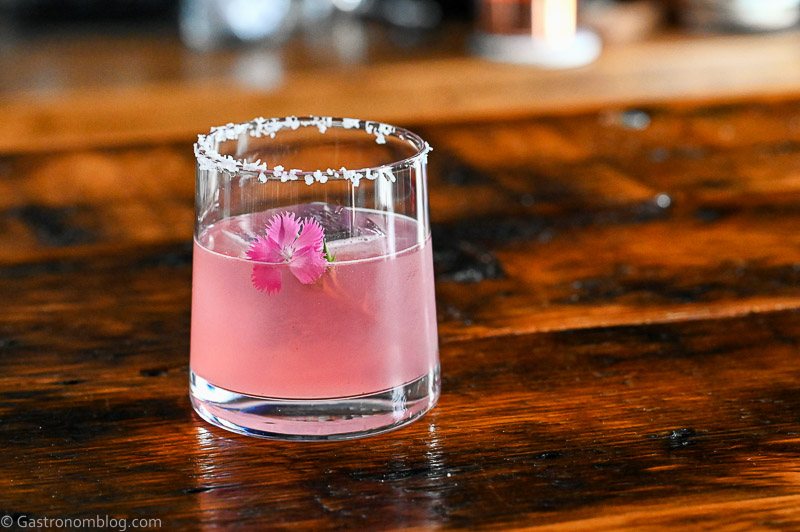 pink blackberry margarita cocktail in rocks glass with salt rim and pink flower garnish