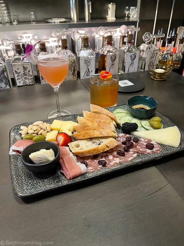 charcuterie with meats and cheeses on slate, cocktails behind on bar top