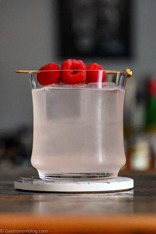 Opaque cocktail in rocks glass with ice. Raspberries on cocktail pick.