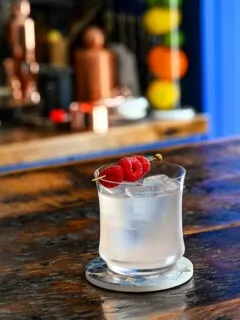 Opaque cocktail in rocks glass with ice. Raspberries on cocktail pick.