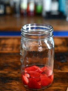 Strawberries in liquid in jar on wood table