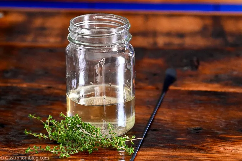 light green thyme simple syrup in jar on wooden table, thyme sprigs by jar