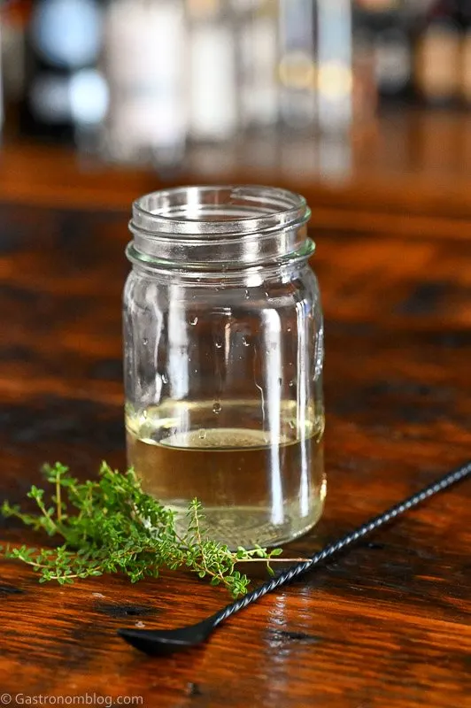 light green thyme simple syrup in jar on wooden table, thyme sprigs by jar