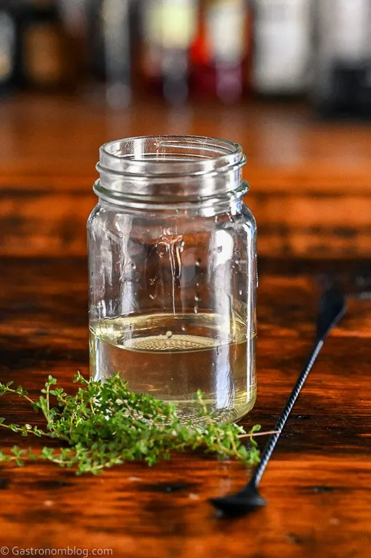 light green thyme simple syrup in jar on wooden table, thyme sprigs by jar