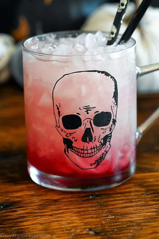 red drink in skull mug, Halloween straws and decor in background
