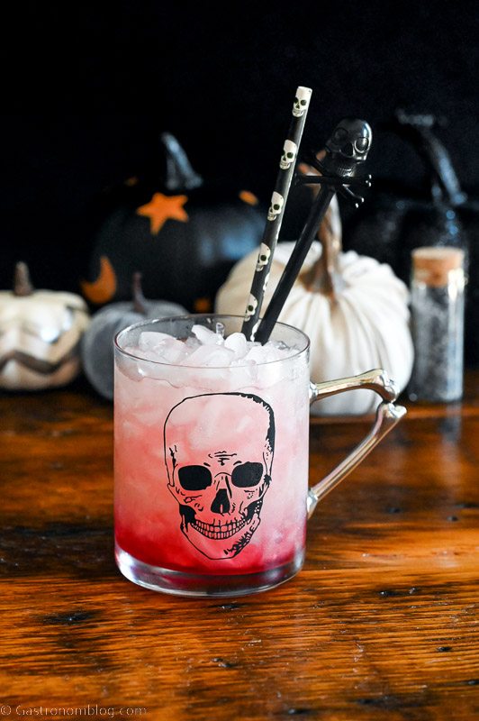 Hocus Pocus cocktail, a red drink in skull mug, Halloween straws and decor in background