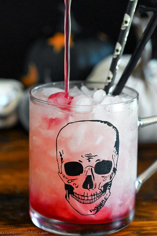 Hocus Pocus cocktail, a red drink in skull mug, Halloween straws and decor in background
