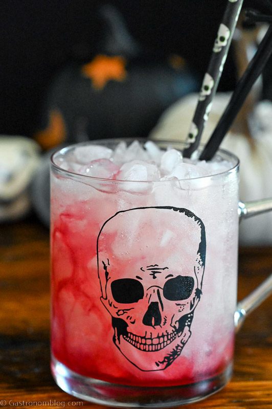 red drink in skull mug, Halloween straws and decor in background