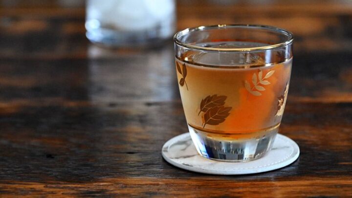 tan maple Old Fashioned cocktail in leaves glass on white coaster on wooden table