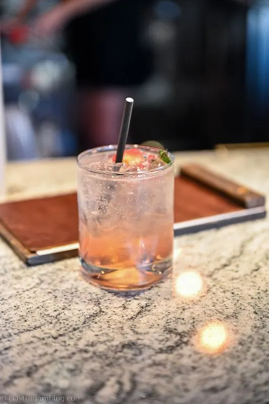 light pink cocktail in a rocks glass with straw. menu behind on bar