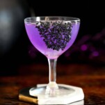 purple cocktail in coupe with black salt garnish, black cauldron and purple glitter sticks behind