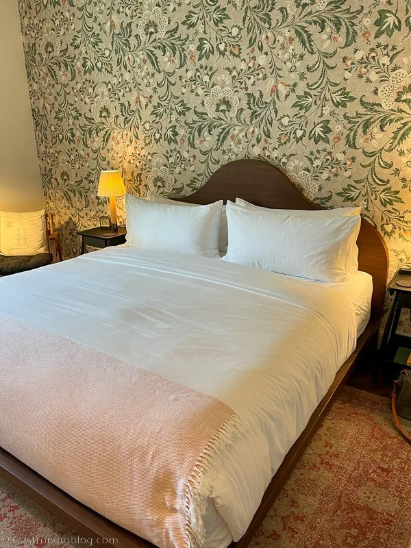 Bed with white sheets at The Pinch Charleston, patterened wallpaper behind