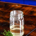 light green thyme simple syrup in jar on wooden table, thyme sprigs by jar