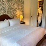 Bed with white sheets at The Pinch Charleston, patterened wallpaper behind