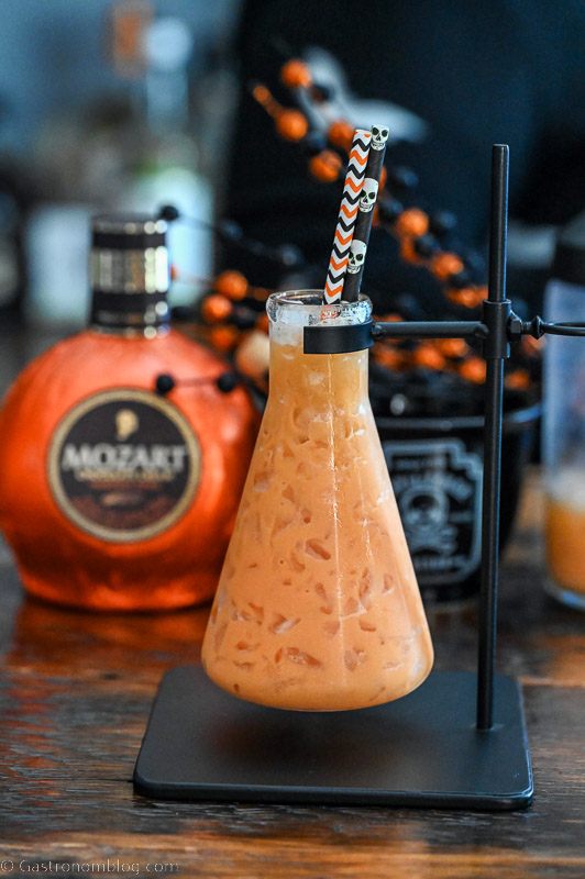 Orange cocktail in beaker, bottle of pumpkin liqueur behind
