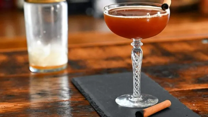 Brown cocktail in coupe with cinnamon stick. On a slate plate.