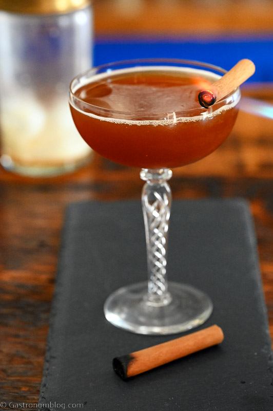 Brown cocktail in coupe with cinnamon stick. On a slate plate.