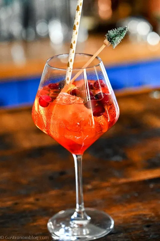 Red Aperol Spritz cocktail in wine glass with cranberries, ice cubes and orange slices.