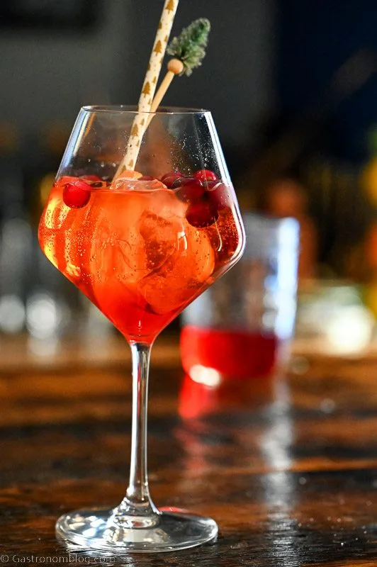 Red Aperol Spritz cocktail in wine glass with cranberries, ice cubes and orange slices.