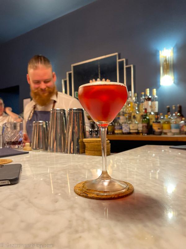 red cocktail in coupe on white marble mantle, bartender in background